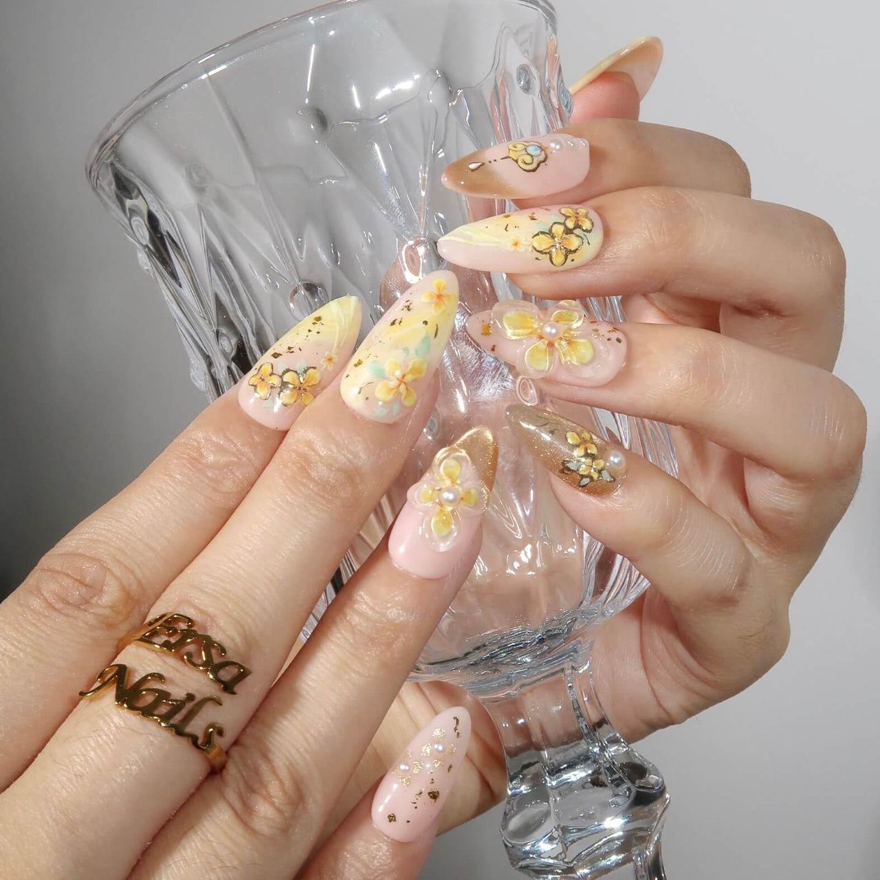 Hand with floral nail design holding a clear glass against a neutral background