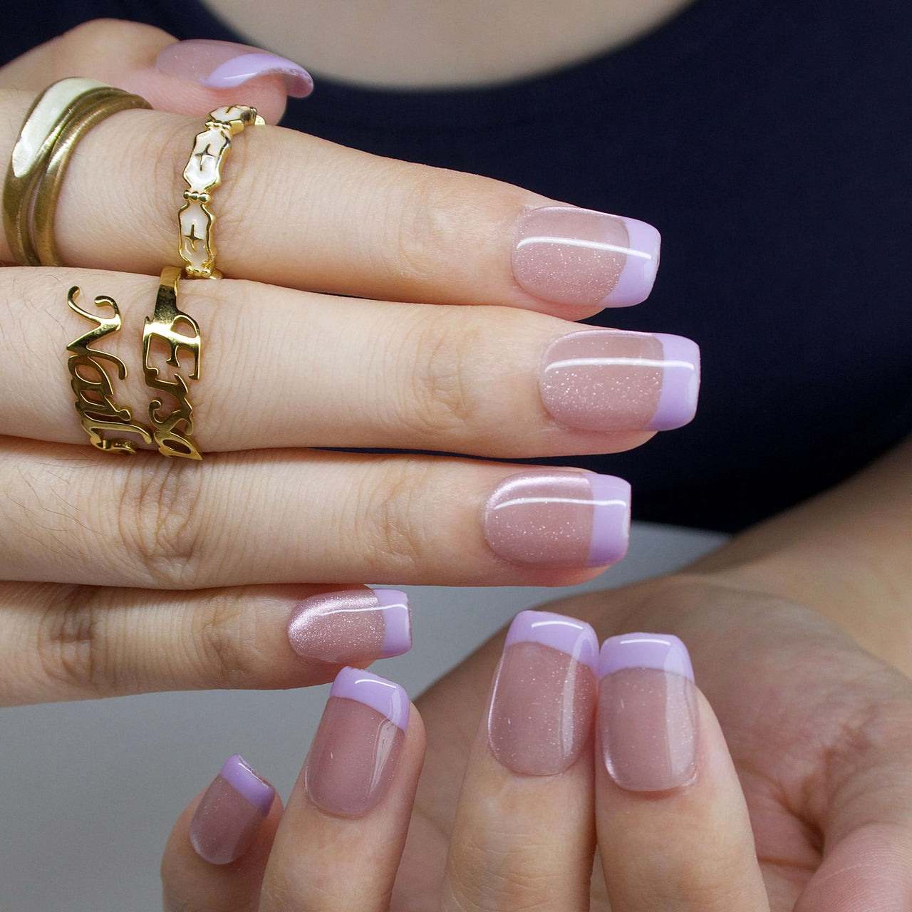 Close-up of hands with pink nail polish and gold rings on a neutral background